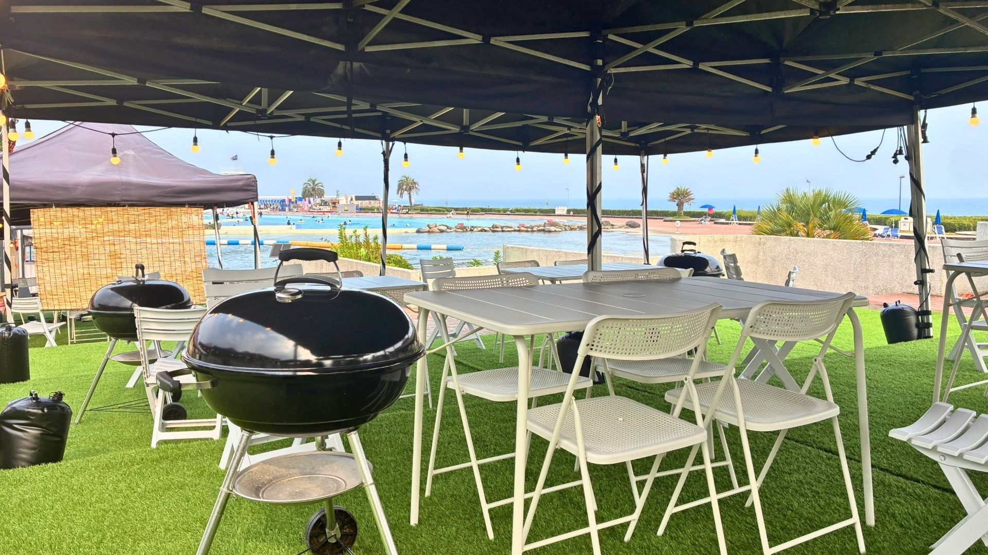 OISO BEACH SIDE BBQのBBQエリア。テント下にテーブル、チェア、炭火グリルが並ぶ様子